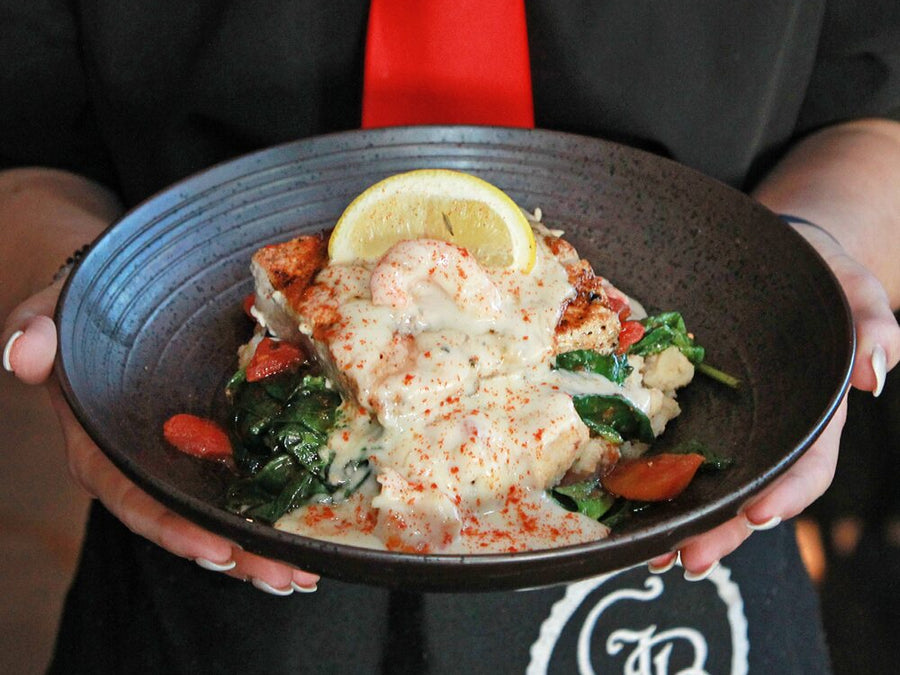 A server holding a Georgia Blue fish entrée with spinach and a lemon wedge